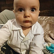 Reagen is registered to the contest to win money with this photo: baby, bed, blanket, candid, child, close_up, clothing, curious, expression, face, head, indoor, infant, person, portrait, reaching_hand, soft_lighting, white_shirt, wide_eyes, young_child