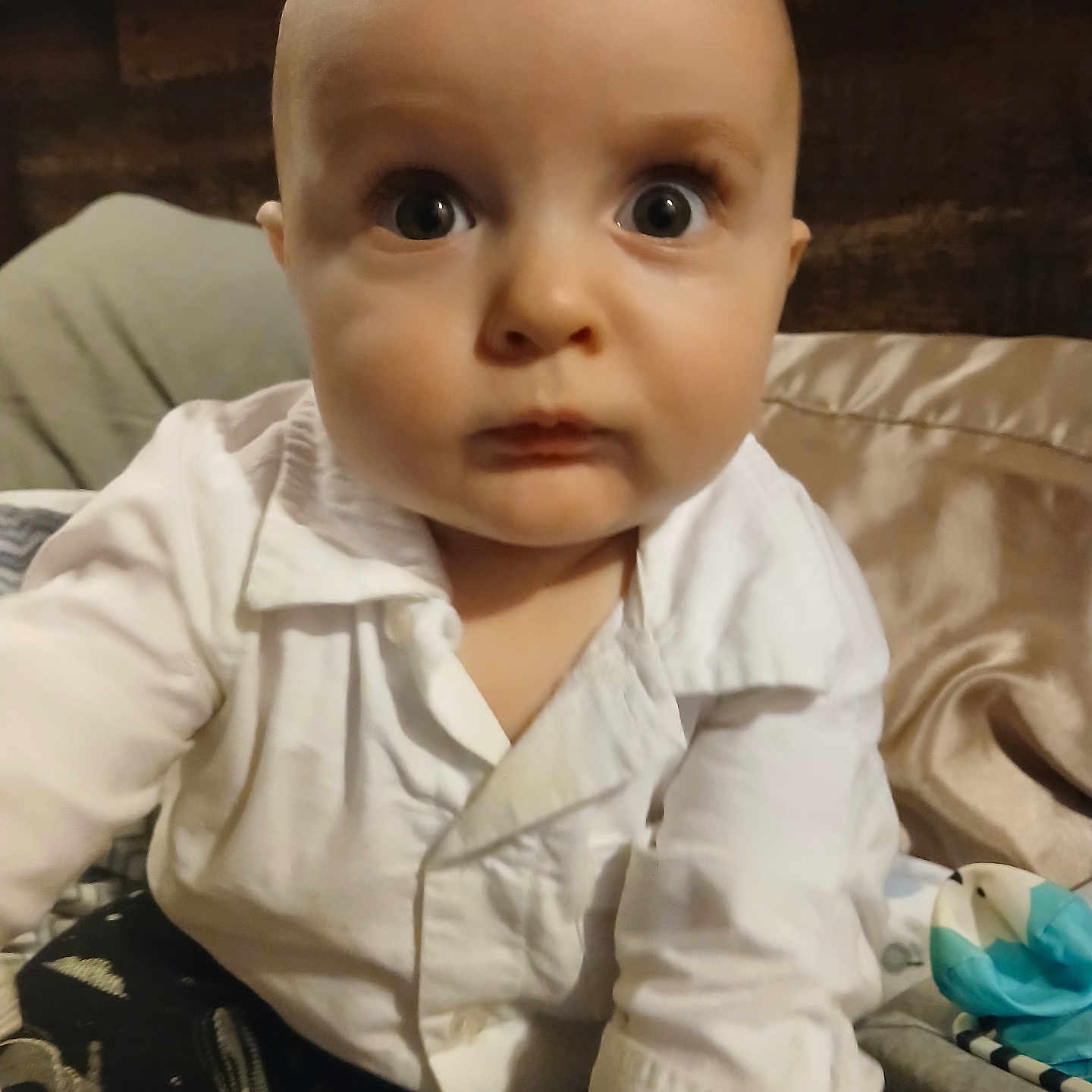 Reagen is registered to the contest to win money with this photo: baby, bed, blanket, candid, child, close_up, clothing, curious, expression, face, head, indoor, infant, person, portrait, reaching_hand, soft_lighting, white_shirt, wide_eyes, young_child