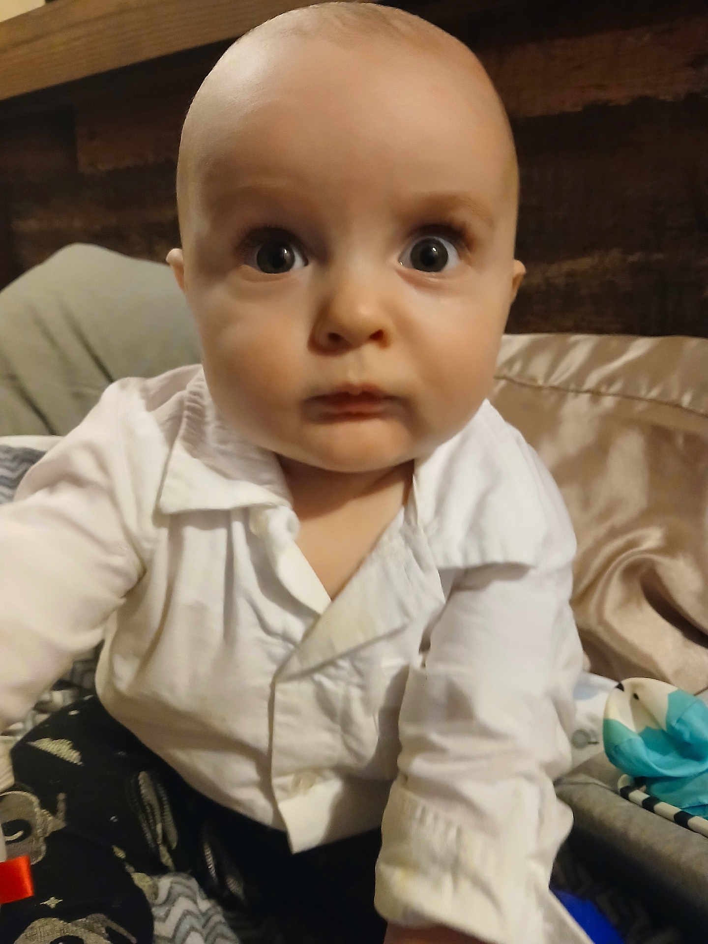 Reagen is registered to the contest to win money with this photo: baby, bed, blanket, candid, child, close_up, clothing, curious, expression, face, head, indoor, infant, person, portrait, reaching_hand, soft_lighting, white_shirt, wide_eyes, young_child