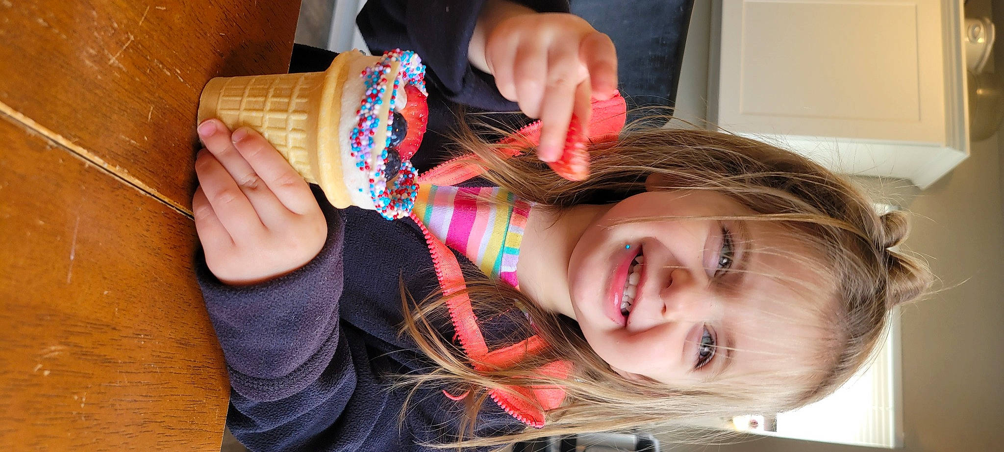 Isabella is registered to the contest to win money with this photo: bangs, brown_hair, child, clothing, eyelash, finger, food, fun, gesture, hand, happy, head, joy, lip, nail, pattern, person, plaid, smile, tableware
