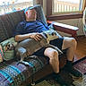Lucy joined the competition — help win amazing prizes! man, dog, couch, nap, indoor, cap, shorts, patterned_fabric, window, daylight, wood_floor, rug, hand, relaxing, pet, furniture, sleeping, home, casual, resting