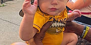 Jaxson joined the competition — help win amazing prizes! baby, child, cap, yellow_shirt, hand, adult_hand, outdoor, grill, people, tattoo, wristband, sitting, concrete, chair, smiling, casual, summer, portrait, daytime, family