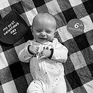 Jaxson is registered to the contest to win money with this photo: baby, infant, smiling, onesie, blanket, checkered_pattern, lying_down, face, hands, feet, valentines_day, milestone, cute, happy, cozy, sleepy, indoor, monochrome, portrait, celebration