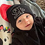 Jaxson is registered to the contest to win money with this photo: baby, infant, beanie, black_clothing, toy, playmat, hand, tattoo, smiling, face, child, indoors, blanket, colorful, cute, lying_down, person, apparel, headwear, skin