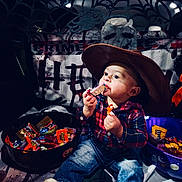 Dakota is registered to the contest to win money with this photo: toddler, child, candy, halloween, costume, cowboy_hat, plaid_shirt, jeans, boots, bowl, decorations, spider_web, skull, pumpkin, indoor, party, celebration, cute, holiday, treats