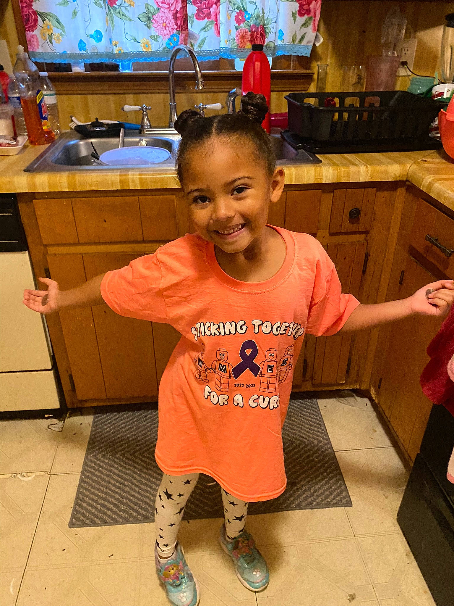 Gwendolyn is registered to the contest to win money with this photo: baby_toddler_clothing, cabinetry, countertop, drawer, floor, flooring, fun, happy, joint, joy, kitchen, kitchen_appliance, orange, person, sink, sleeve, smile, standing, t_shirt, tap