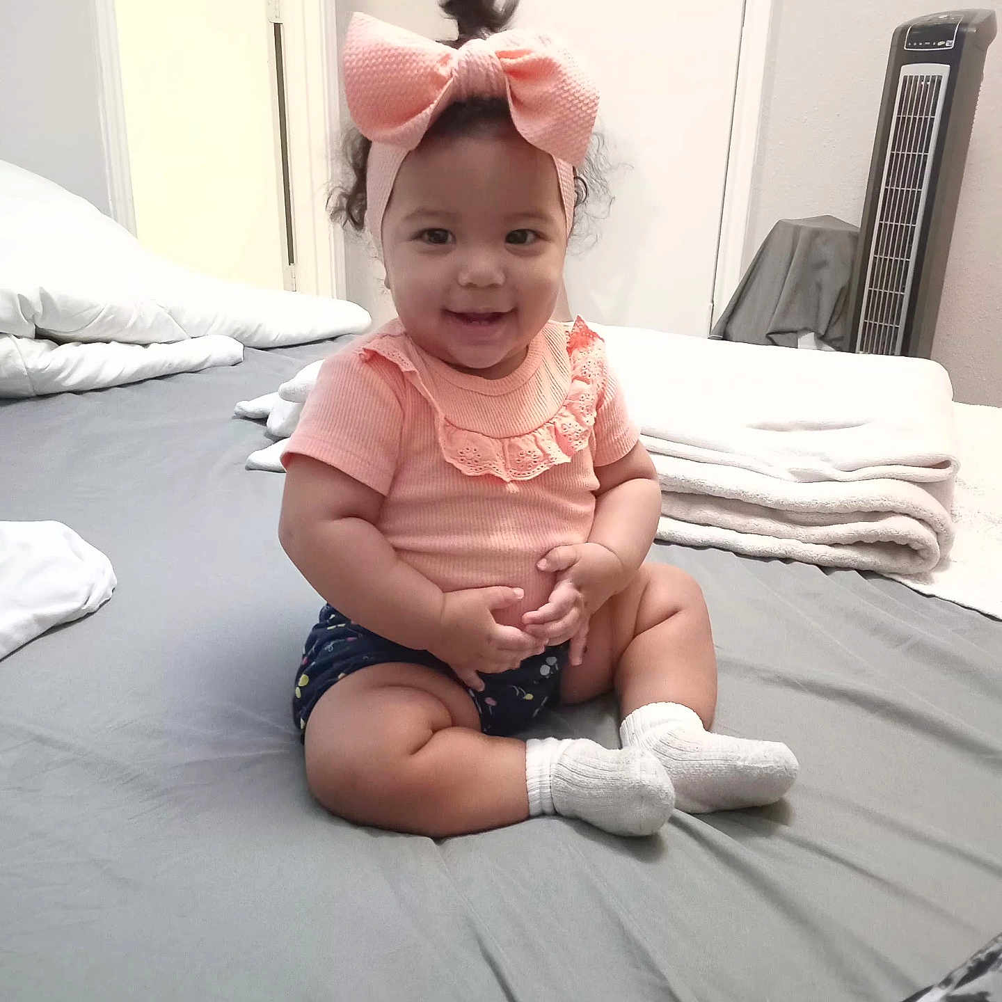 Danna Naranjo joined the competition — help win amazing prizes! baby, child, indoor, bed, blanket, fan, headband, pink_bow, smiling, cute, sitting, clothing, white_socks, shorts, happy, portrait, person, home, toddler, furniture