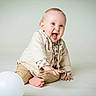 baby, child, tongue_out, blue_eyes, sitting, balloon, playful, cute, light_background, beige_clothing, infant, happy, studio, portrait, smiling, barefoot, buttoned_shirt, long_sleeves, indoor, young
