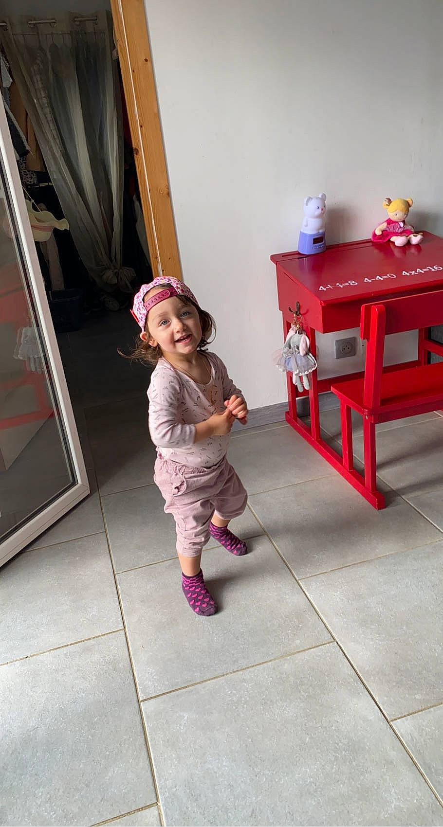 Léa-marie a rejoint le concours — aidez-le/la à gagner de superbes lots ! baby_toddler_clothing, child, door, floor, flooring, fun, hardwood, hat, headwear, joy, leg, magenta, person, pink, red, room, smile, snapshot, standing, stool