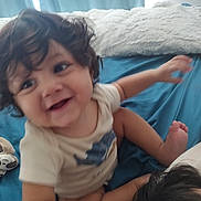 Aziel joined the competition — help win amazing prizes! toddler, child, curly_hair, smiling, bed, pillow, blue_bedspread, indoor, candid, happy, person, clothing, skin, face, arm, foot, toy, blanket, motion_blur, home