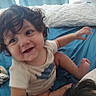 toddler, child, curly_hair, smiling, bed, pillow, blue_bedspread, indoor, candid, happy, person, clothing, skin, face, arm, foot, toy, blanket, motion_blur, home