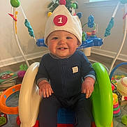 Nathan is registered to the contest to win money with this photo: baby, child, smile, hat, indoor, toys, slide, colorful, happy, person, seat, blue_clothing, window, plant, floor, play_area, home, furniture, daylight, cheerful