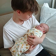 Nathan joined the competition — help win amazing prizes! child, baby, boy, infant, couch, white_tshirt, swaddle, animal_print, indoor, pillow, love, family, tenderness, sibling, holding, seated, cozy, portrait, looking, home