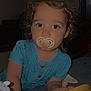 toddler, child, pacifier, curly_hair, blue_dress, wooden_object, indoor, face, portrait, young_child, person, baby, candid, expression, closeup, cute, holding, looking, home, soft_lighting