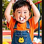 child, toddler, smiling, happy, denim_overalls, orange_shirt, playground, outdoor, cute, face, hair, joyful, young, person, fun, colorful, daylight, casual_clothing, yellow_ball, park