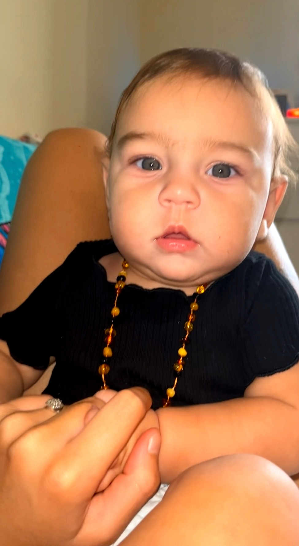 Inaya participe au concours pour gagner de l'argent avec cette photo : baby, child, infant, face, hand, holding, black_clothing, necklace, beads, skin, eyes, person, portrait, closeup, cute, indoor, human, expression, young, chubby_cheeks
