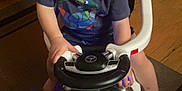 Willie joined the competition — help win amazing prizes! child, toddler, toy_car, indoor, steering_wheel, footwear, clothing, floor, car_toy, person, young_child, head, eyes, expression, sitting, wood_floor, furniture, chair, casual, play