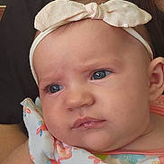 Olivia joined the competition — help win amazing prizes! baby, infant, headband, bow, tattoo, arm, person, clothing, colorful, floral, expression, portrait, skin, face, blue_eyes, cute, indoor, holding, adult, closeup