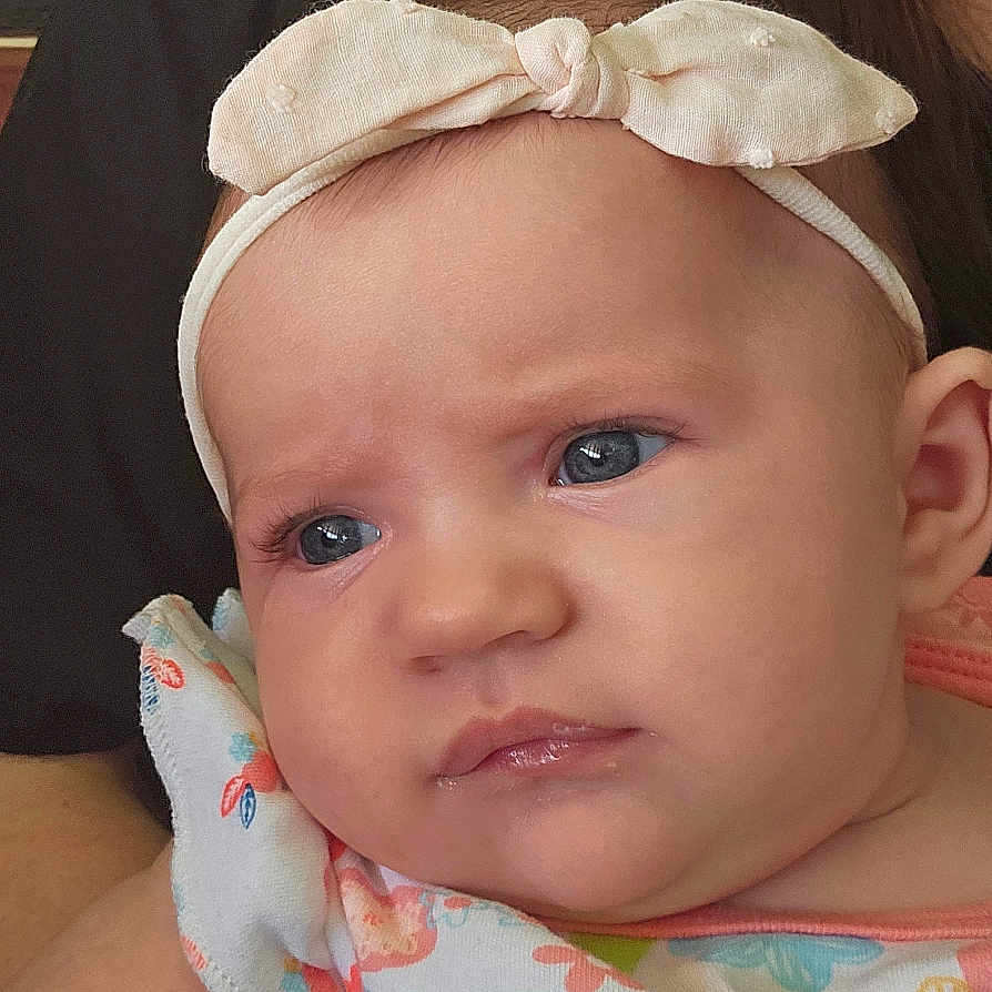 Olivia joined the competition — help win amazing prizes! baby, infant, headband, bow, tattoo, arm, person, clothing, colorful, floral, expression, portrait, skin, face, blue_eyes, cute, indoor, holding, adult, closeup