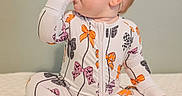 Bexley is registered to the contest to win money with this photo: baby, child, onesie, bow_pattern, headband, thumb_sucking, sitting, soft_surface, quilted_blanket, indoor, cute, infant, portrait, clothing, foot, hand, face, looking_sideways, light_skin, calm_background