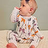 baby, child, onesie, bow_pattern, headband, thumb_sucking, sitting, soft_surface, quilted_blanket, indoor, cute, infant, portrait, clothing, foot, hand, face, looking_sideways, light_skin, calm_background