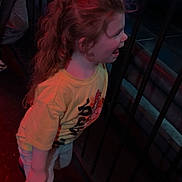 Kailynn is registered to the contest to win money with this photo: child, curly_hair, yellow_shirt, metal_railing, neon_lights, indoor, person, profile_view, excitement, standing, casual_clothing, long_hair, red_boots, dark_background, colorful_lighting, playful, young_child, smiling, side_view, fun