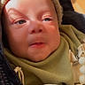 baby, child, face, hat, knit_hat, jacket, green_bib, mitten, dinosaur_pattern, sunlight, shadow, close_up, infant, cute, warm_clothing, indoor, soft_light, expression, person, bundle