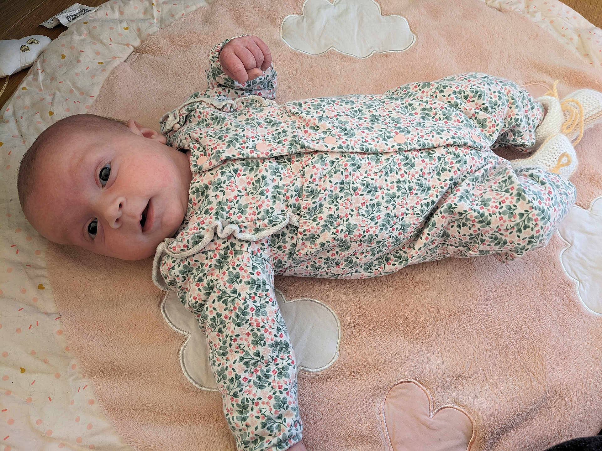 Clara participe au concours pour gagner de l'argent avec cette photo : baby, infant, onesie, floral_pattern, blanket, soft_texture, heart_shape, cloud_shape, lying_down, curious_expression, indoor, floor, cute, child, newborn, knitted_booties, pale_skin, small_hands, baby_clothes, portrait