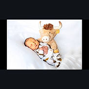 Walker is registered to the contest to win money with this photo: baby, newborn, sleeping, stuffed_animal, bull, toy, white_background, infant, cute, soft, cozy, child, peaceful, resting, pajamas, patterned_clothing, hands, face, lying_down, indoors
