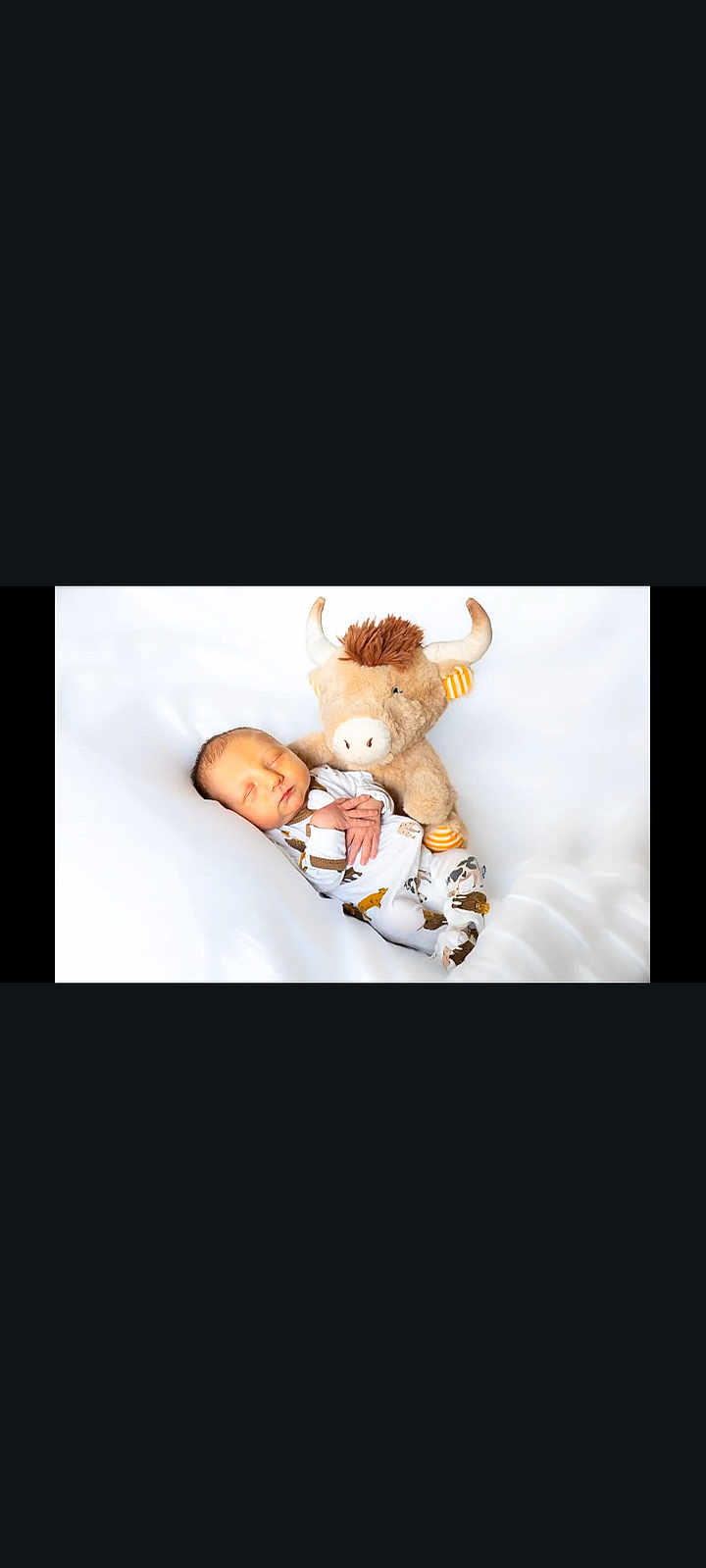 Walker is registered to the contest to win money with this photo: baby, newborn, sleeping, stuffed_animal, bull, toy, white_background, infant, cute, soft, cozy, child, peaceful, resting, pajamas, patterned_clothing, hands, face, lying_down, indoors