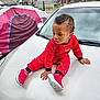 Tayzon is registered to the contest to win money with this photo: child, toddler, red_clothing, sneakers, car, car_hood, outdoor, tent, fence, curly_hair, side_view, person, casual, daylight, urban, concrete, curious, sitting, baby, head