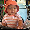 Giovanni joined the competition — help win amazing prizes! baby, child, orange_hat, striped_shirt, high_chair, menu, indoor, restaurant, table, colorful_chairs, curious, person, face, smiling, casual_clothing, bright_light, daylight, hand, seated, young_child