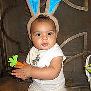 Giovanni joined the competition — help win amazing prizes! baby, bunny_ears, toy, carrot, child, cute, costume, face, floor, indoor, infant, person, portrait, sitting, tile_floor, white_clothing, headwear, playful, smiling, young_child