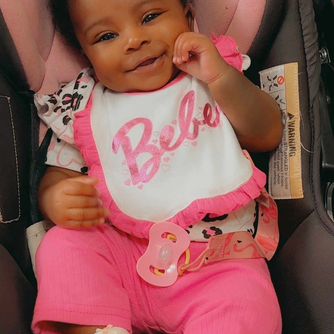 Demyia joined the competition — help win amazing prizes! baby, bib, car_seat, child, clothing, curly_hair, cute, face, footwear, happy, indoors, infant, pacifier, person, pink_clothing, portrait, seat_belt, smiling, socks, young_child