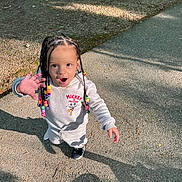 Ryah is registered to the contest to win money with this photo: asphalt, beads, braided_hair, child, cute, daylight, fashion, gesture, happy, mickey_mouse, outdoor, park, person, playful, shadow, shorts, smiling, sneakers, sweatshirt, young