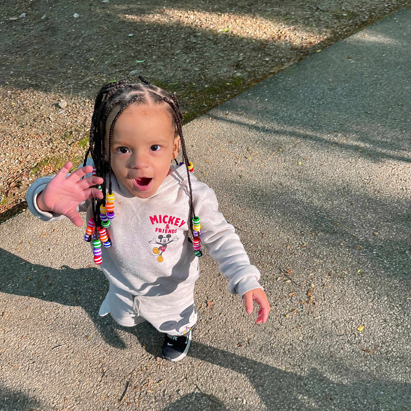 Ryah is registered to the contest to win money with this photo: asphalt, beads, braided_hair, child, cute, daylight, fashion, gesture, happy, mickey_mouse, outdoor, park, person, playful, shadow, shorts, smiling, sneakers, sweatshirt, young