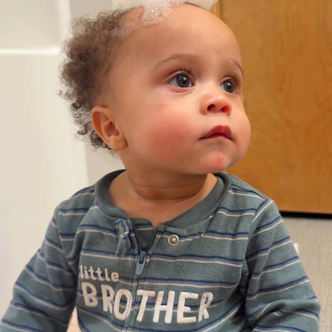 Siylas is registered to the contest to win money with this photo: baby, blue, bubbles, child, clothing, curly_hair, door, expression, face, floor, foam, green, hand, indoor, long_sleeve, looking_away, sitting, striped_pajamas, toddler, zipper