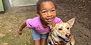 Madison is registered to the contest to win money with this photo: animal, casual_clothing, child, crocs, dog, fence, footwear, friendship, happy, harness, leash, nature, outdoor, path, pet, playful, shorts, smiling, tree, tshirt