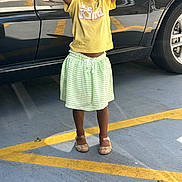 Madison is registered to the contest to win money with this photo: arms_raised, braided_hair, car, casual_clothing, child, concrete, daylight, footwear, green_skirt, happy, outdoor, parking_lot, person, reflection, smiling, sparkly_shoes, standing, toddler, vehicle, yellow_tshirt