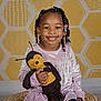 Madison joined the competition — help win amazing prizes! beads, bee_toy, braids, candid, child, cute, girl, happy, honeycomb_pattern, indoor, kids, patterned_wall, person, plush_toy, portrait, purple_dress, sitting, smile, toy, woven_mat