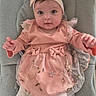 adorable, baby, baby_seat, child, cozy, cute, expression, floral_embroidery, gray_cushion, headband, indoors, infant, looking_at_camera, pink_dress, portrait, sitting, small_hands, soft_lighting, white_tights, young_child