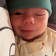 Xavier joined the competition — help win amazing prizes! baby, infant, smiling, winking, beanie, green_hat, onesie, cozy, cute, sleepwear, patterned_clothing, pillow, snuggling, indoors, face, headwear, closeup, soft_lighting, child, portrait
