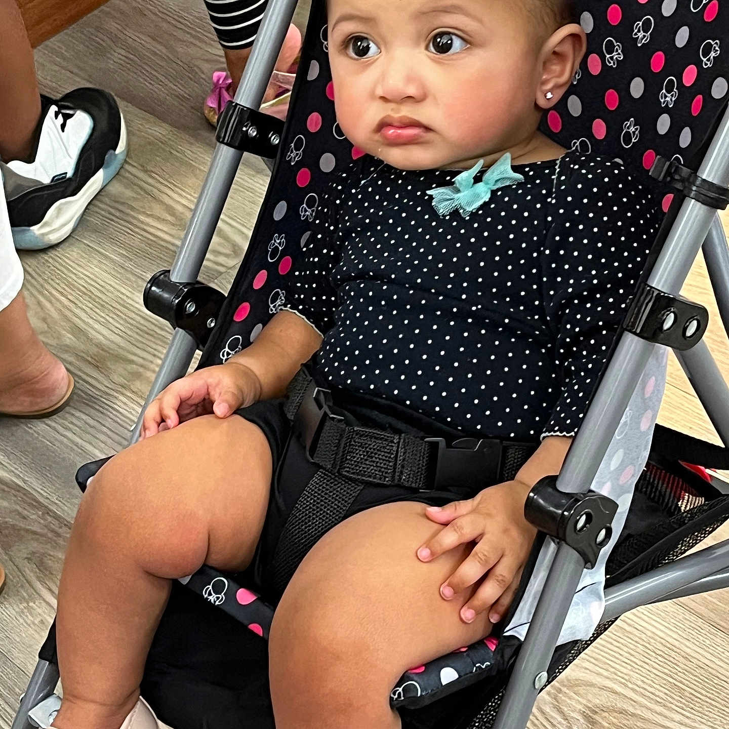 Mande is registered to the contest to win money with this photo: baby, belt, black_clothing, bow, child, curious, earrings, expression, flooring, footwear, hand, indoor, legs, metal_frame, person, polka_dot, seated, shoes, stroller, toddler