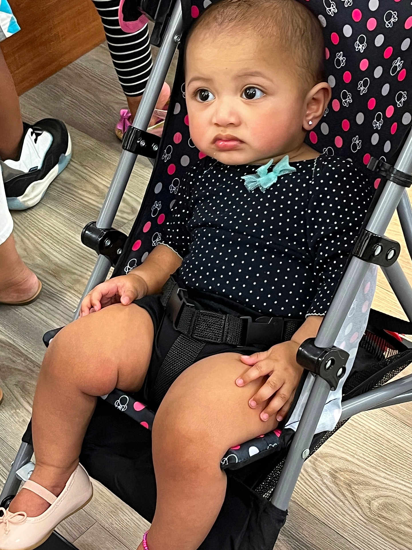 Mande is registered to the contest to win money with this photo: baby, toddler, child, stroller, polka_dot, black_clothing, bow, earrings, shoes, indoor, flooring, legs, curious, seated, expression, hand, footwear, belt, metal_frame, person