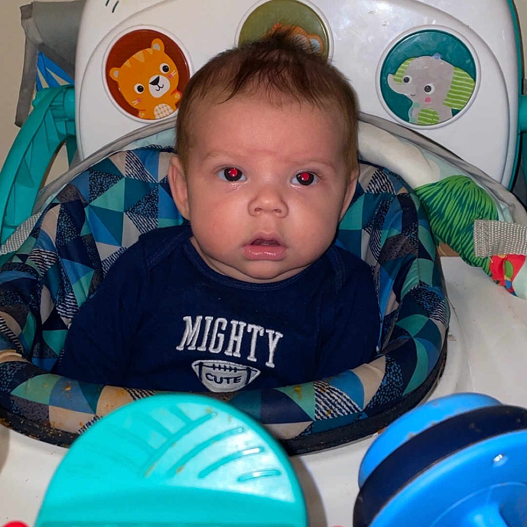 Easton is registered to the contest to win money with this photo: baby, background, blue, child, clothing, colorful, cute, expression, face, green, indoor, person, plastic, red, red_eye, seat, toy, walker, yellow, young