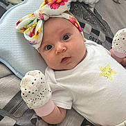 Ashley joined the competition — help win amazing prizes! baby, blanket, child, closeup, curious_expression, cute, floral, hand, headband, indoor, infant, lying_down, mittens, newborn, patterned_blanket, person, small_hands, soft_lighting, star_print, white_onesie