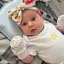baby, blanket, child, closeup, curious_expression, cute, floral, hand, headband, indoor, infant, lying_down, mittens, newborn, patterned_blanket, person, small_hands, soft_lighting, star_print, white_onesie