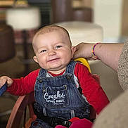 Helio participe au concours pour gagner de l'argent avec cette photo : baby, child, smiling, denim_overalls, red_shirt, high_chair, indoor, hand, person, cute, happy, seated, furniture, toy, plush_toy, portrait, face, young_child, casual_clothing, support