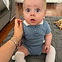 baby, child, blue_outfit, knitted_clothing, white_socks, knee_high_socks, sitting, wide_eyes, surprised_expression, hand, adult_hand, rug, gray_rug, indoor, wooden_floor, couch, stuffed_toy, giraffe_toy, person, portrait