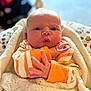 baby, infant, face, hands, blanket, clothing, orange_stripes, expression, cute, newborn, wrapped, cozy, portrait, indoor, soft_light, skin, person, closeup, warm, child